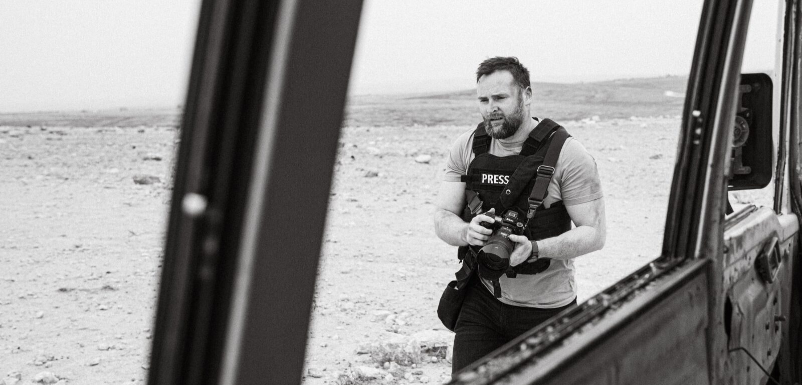 Daniel Wheeler in press body armor seen through the window of a bombed-out bus in the Middle East.